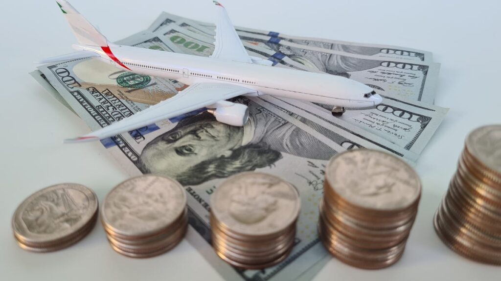 a model of an airplane sits upon several $100 bills with stacks of coins in front of it
