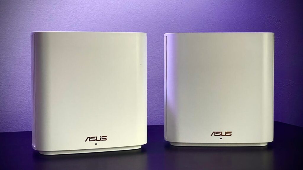Two white Asus routers sit on a table with a purple backdrop.