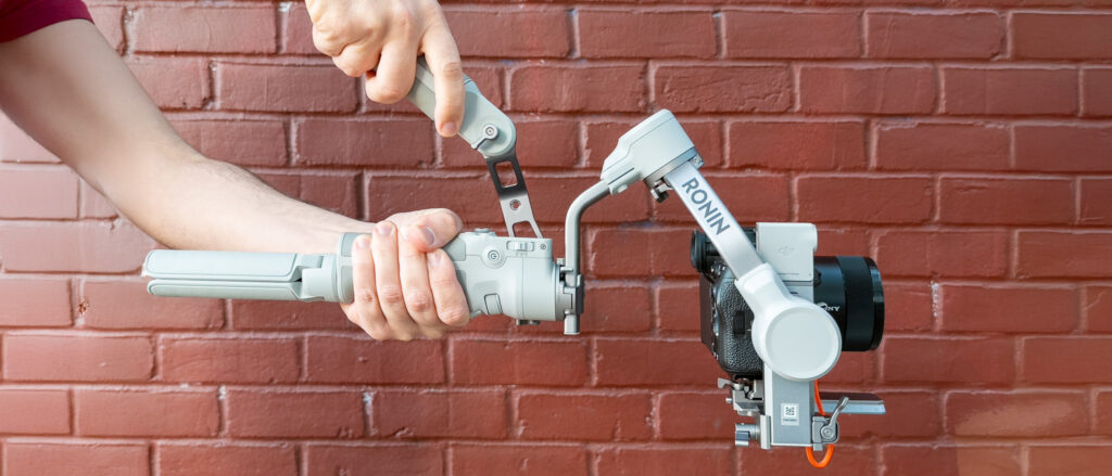 DJI RS 4 Mini review: Smarter, Faster, Still Travel-Ready Holding the DJI RS4 Mini against a brick wall