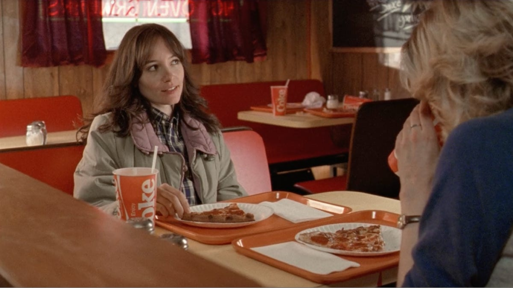 a screen capture from the movie The House of the Devil, showing Sam, played by Jocelin Donahue, sitting across from Megan, played by Greta Gerwig, at a pizza restaurant in the 1980s