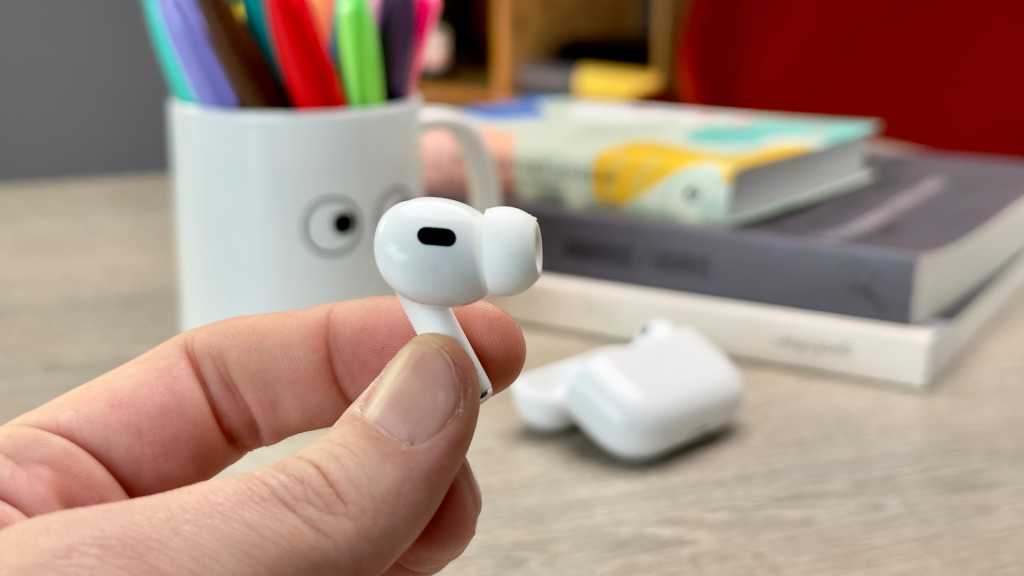Unreleased Apple product in mysterious code could be new AirPods Holding the AirPods Pro (2022) earbud with case in the background