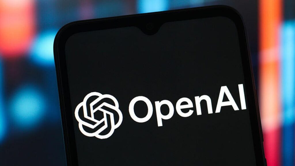 Why You Should Care About OpenAI’s New $200 Million Defense Department Deal OpenAI name and logo on a smartphone in front of a red and blue lit background