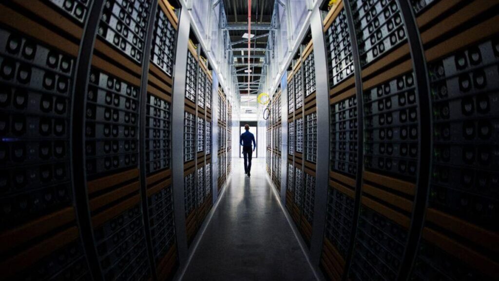 Data Centers Are ‘AI Factories.’ Google and Meta Are Spending Big Bucks to Build Them A silhouette of a person walking between two looming walls of servers in a data center