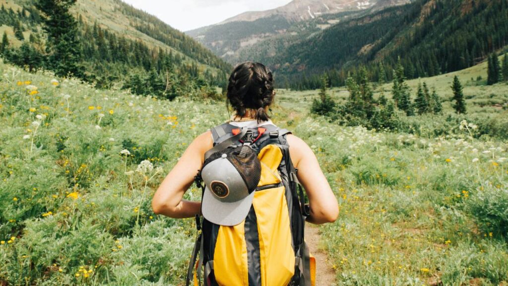 A woman wearing a yellow backpack looking out over fields and mountains