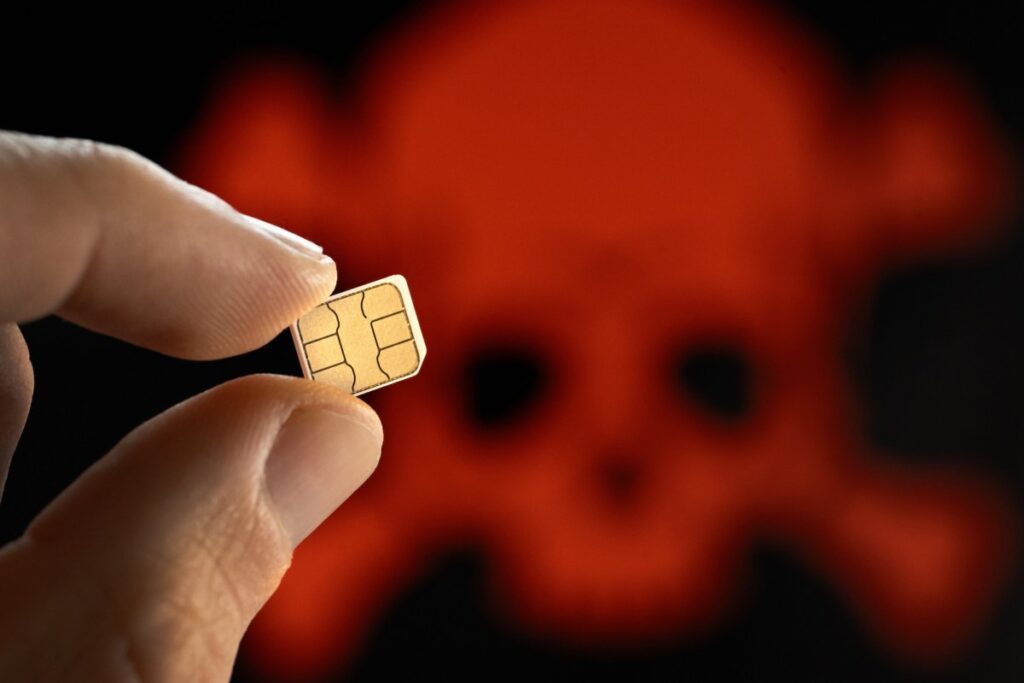 A close up shot of a person holding a SIM card, with a skull in the background to demonstrate SIM hack
