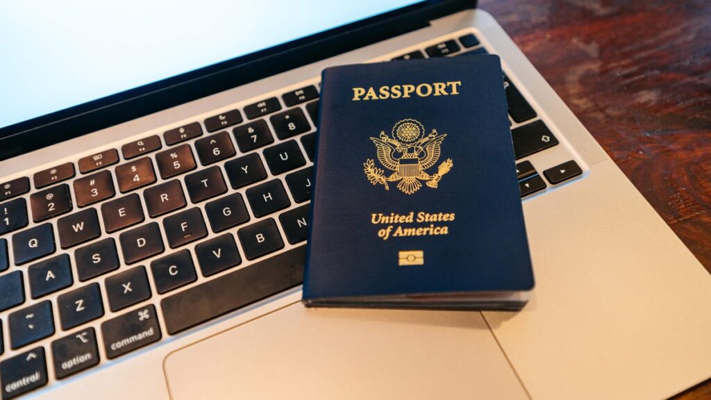 a blue US passport book sits on the keyboard of a laptop computer