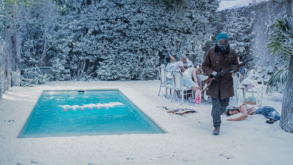 When Will You See AI-Generated Content on Netflix? It’s Possible You Already Have A man with a gun passes a frozen swimming pool and a table full of people in a still frame from the show El Eternauta