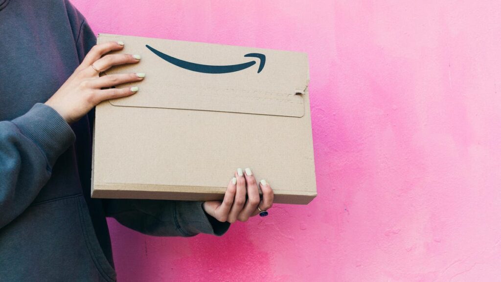 body of young woman holding an amazon packet on pink background.