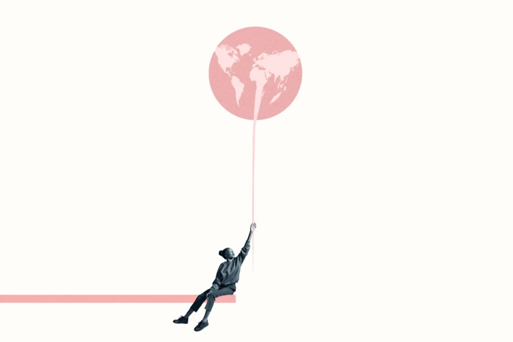 Young woman holding at large pink balloon with world map while sitting on ramp against white background