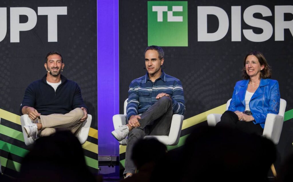 Three speakers talk on a stage with a black backdrop.